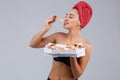 A girl is in black underwear and wrapped in a towel on head, eating an appetizing piece of pizza.