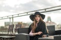 Girl in a black wide-brimmed hat and cloak sitting on the terrace of the restaurant