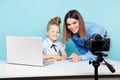 Girl blogger recording vlog on the camera sitting with laptop and mother helping her to look good.