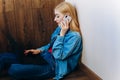 Girl with blond hair in denim clothes working at home with a laptop and talking on the phone. Royalty Free Stock Photo