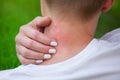 Girl with blond hair, sitting with his back turned and scratching bitten, red, swollen neck skin from mosquito bites in the summer