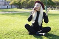 A girl with blond hair is talking on the phone while sitting on the grass in a park. Emotion is joy Royalty Free Stock Photo