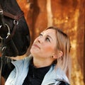 Girl blonde in blue quilted vest with ponytail plays with her horse, portraits of the woman with focus on her head close-up. Royalty Free Stock Photo