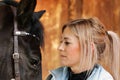 Girl blonde in blue quilted vest with ponytail plays with her horse, portraits of the woman with focus on her head close-up. Royalty Free Stock Photo