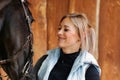 Girl blonde in blue quilted vest with ponytail plays with her horse, portraits of the woman with focus on her head close-up. Royalty Free Stock Photo