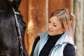 Girl blonde in blue quilted vest with ponytail plays with her horse, portraits of the woman with focus on her head close-up. Royalty Free Stock Photo