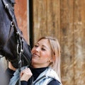 Girl blonde in blue quilted vest with ponytail plays with her horse, portraits of the woman with focus on her head close-up. Royalty Free Stock Photo