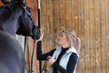 Girl blonde in blue quilted vest with ponytail plays with her horse, portraits of the woman with focus on her head close-up. Royalty Free Stock Photo