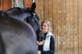 Girl blonde in blue quilted vest with ponytail plays with her horse, portraits of the woman with focus on her head close-up. Royalty Free Stock Photo