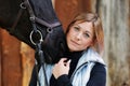 Girl blonde in blue quilted vest with ponytail plays with her horse, portraits of the woman with focus on her head close-up. Royalty Free Stock Photo