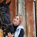 Girl blonde in blue quilted vest with ponytail plays with her horse, portraits of the woman with focus on her head close-up. Royalty Free Stock Photo