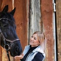 Girl blonde in blue quilted vest with ponytail plays with her horse, portraits of the woman with focus on her head close-up. Royalty Free Stock Photo