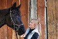 Girl blonde in blue quilted vest with ponytail plays with her horse, portraits of the woman with focus on her head close-up. Royalty Free Stock Photo