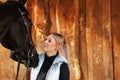 Girl blonde in blue quilted vest with ponytail plays with her horse, portraits of the woman with focus on her head close-up. Royalty Free Stock Photo