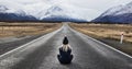 Girl with blonde hair wearing a hat sits in the middle of the road in New Zealand