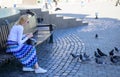 Girl blonde woman relaxing city square and feeding pigeons. Woman tourist or citizen toss crumbs for pigeons. Group