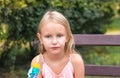 Girl, blonde 6-7 years old, with a sad face, sits on a park bench and eats popsicles, portrait of a child in nature who eats ice c Royalty Free Stock Photo