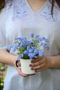 A girl in a blouse with delicate embroidery holds in her hands a white mug with forget-me-nots. Spring concept