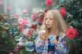 Girl blowing rainbow color soap bubbles in the bush of roses