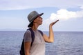 Girl blows up a cloud above sea. Model posing on tropical sea background. Marine traveler in sun hat.