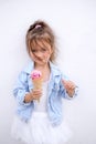 A girl in blue denim jacket and white skirt eats ice cream in waffle cone