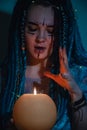 Girl with blue dreadlocks conjures at night in a dark room, candle fire and a cow skull. Royalty Free Stock Photo