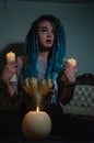 Girl with blue dreadlocks conjures at night in a dark room, candle fire and a cow skull . Royalty Free Stock Photo
