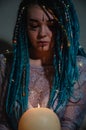 Girl with blue dreadlocks conjures at night in a dark room, candle fire and a cow skull.