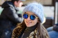 A girl in blue glasses and a warm plump gray hat posing outside in the cold season. portrait of a beautiful girl in glasses