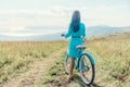 Girl with blue hair standing with bicycle on country road.