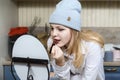 Girl in a blue hat paints her lips in front of the mirror at home in the kitchen Royalty Free Stock Photo