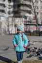 A girl in a blue jacket poses outside in front of a flock of city pigeons. A five-year-old child with long pigtails. Blurred image