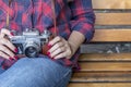 Girl in blue jeans and checkered shirt is sitting on the wooden bench and holding an old film camera in her hands. Royalty Free Stock Photo