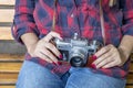 Girl in blue jeans and checkered shirt is sitting on the wooden bench and holding an old film camera in her hands. Royalty Free Stock Photo