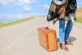 A girl in blue jeans, a poncho, a black leather hat with an old brown suitcase in her hands is on the road. Royalty Free Stock Photo