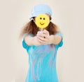 Girl in blue shirt and cap with two tails holds in front of a big yellow candy