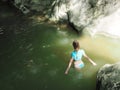 A girl in a blue swimsuit walks into the muddy green water of a rocky gorge Royalty Free Stock Photo
