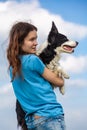 A girl in a blue T-shirt holds a black and white border collie dog in her arms. Portrait against a bright blue sky with Royalty Free Stock Photo