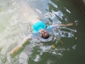 A girl in a blue top swims face up in muddy water with her arms outstretched to the sides