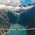 Girl in blue tshirt and a yellow hat sitting on a suspension bridge above the Alps. Freedom and adventure concept. Touristic