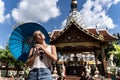 Girl with a blue umbrella in her hands with a comfortable expression sunbathing in front of a Buddhist temple Royalty Free Stock Photo