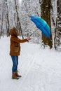Girl with blue umbrella in snowy forest with strong wind. Snowfall concept. Woman under wet snow rain in winter park. Royalty Free Stock Photo