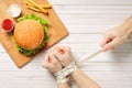 A girl with bound hands measuring tape, In front of a hamburger lying on a table.male hands holding a measuring tape without