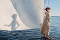 The girl on the bow of a sailing ship against the blue sky on a sunny day casts a shadow on the sail Royalty Free Stock Photo