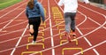 Girl and boy running over small yellow hurdles in lane on a track in the cold