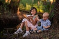 Girl and boy are sitting on the bank of river, launching white paper origami boat into the water