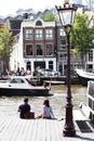 Girl and boy are sitting on a pier watching boats pass py on Amstel.