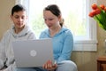 girl and boy teenagers doing homework or watching movies on laptop sitting on small sofa against window boy bit lip Royalty Free Stock Photo