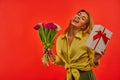 Girl brags showing tongue in a yellow blouse with a bouquet of tulips and a white box tied with red ribbon Royalty Free Stock Photo