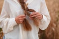 A girl braids her hair in a wheat field